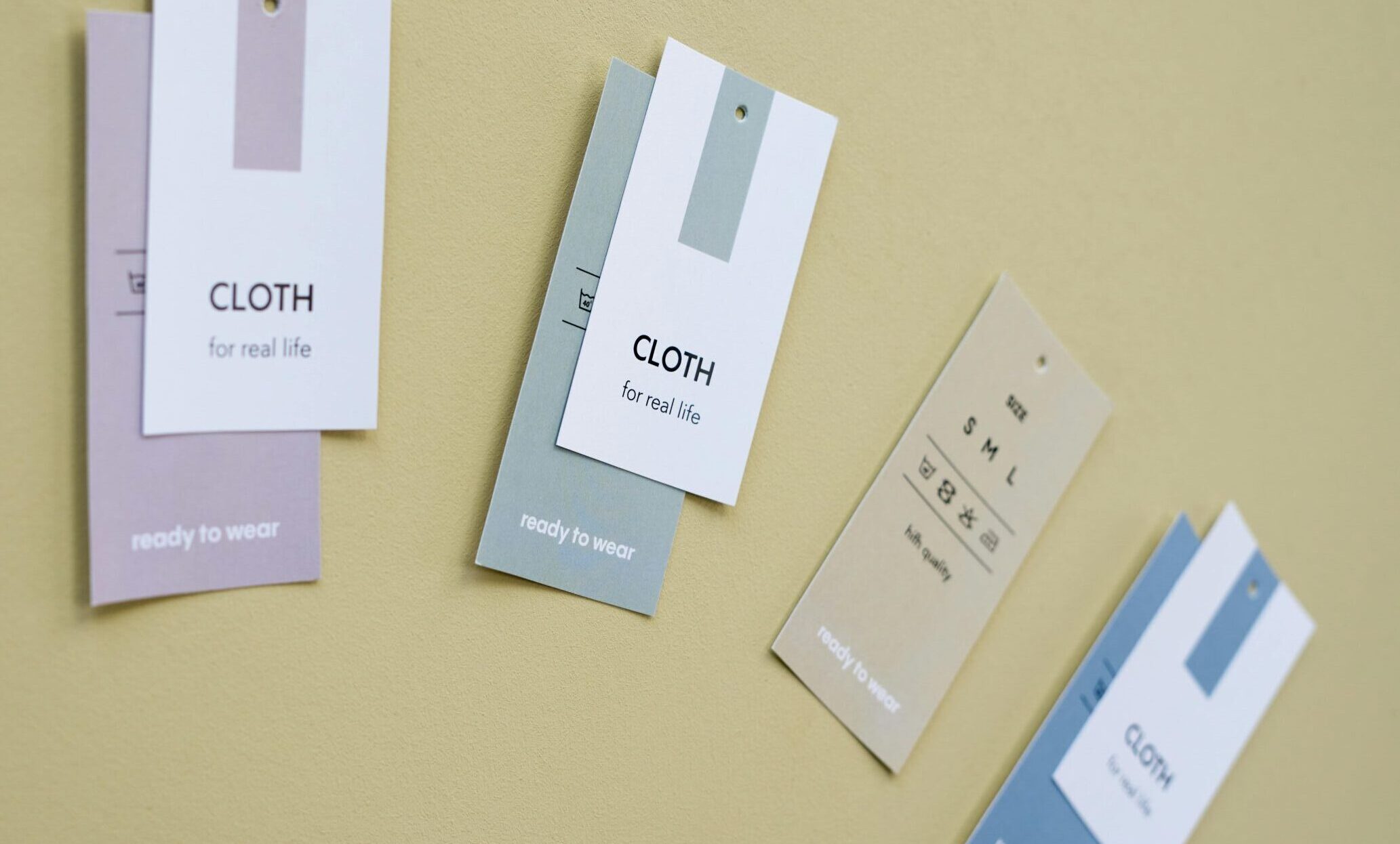 Close-up of minimalist clothing tags placed on a soft yellow surface, showcasing fashion and branding concepts.
